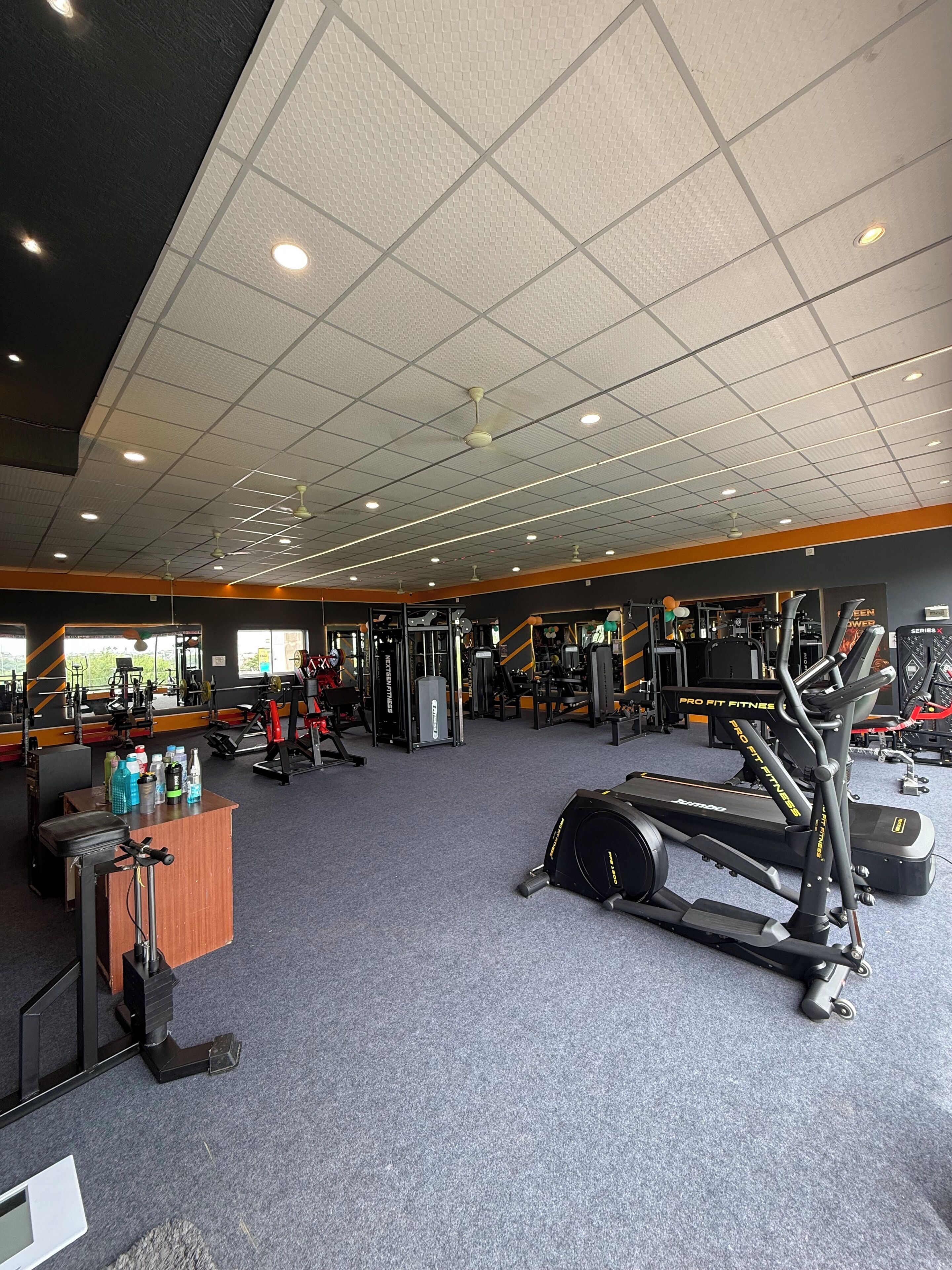 A gym with various exercise equipment, a reception desk, and a ceiling with recessed lighting.
