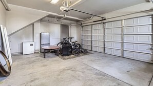 En garage med betongulv, loftsvifte, køleskab, bord og to cykler.
