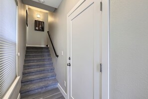Uma escadaria com corrimão, uma porta com puxador e um aplique de parede.