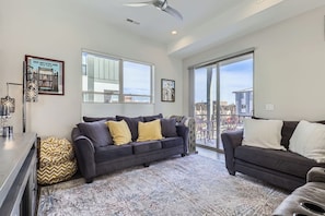 A modern living room with a dark grey sofa, yellow cushions, and a patterned rug. There is a framed poster on the wall and a ceiling fan. - Walk to Olde Town Arvada | 2 Ensuite Bedrooms | Garage | Sleeps 5 (Arvada)