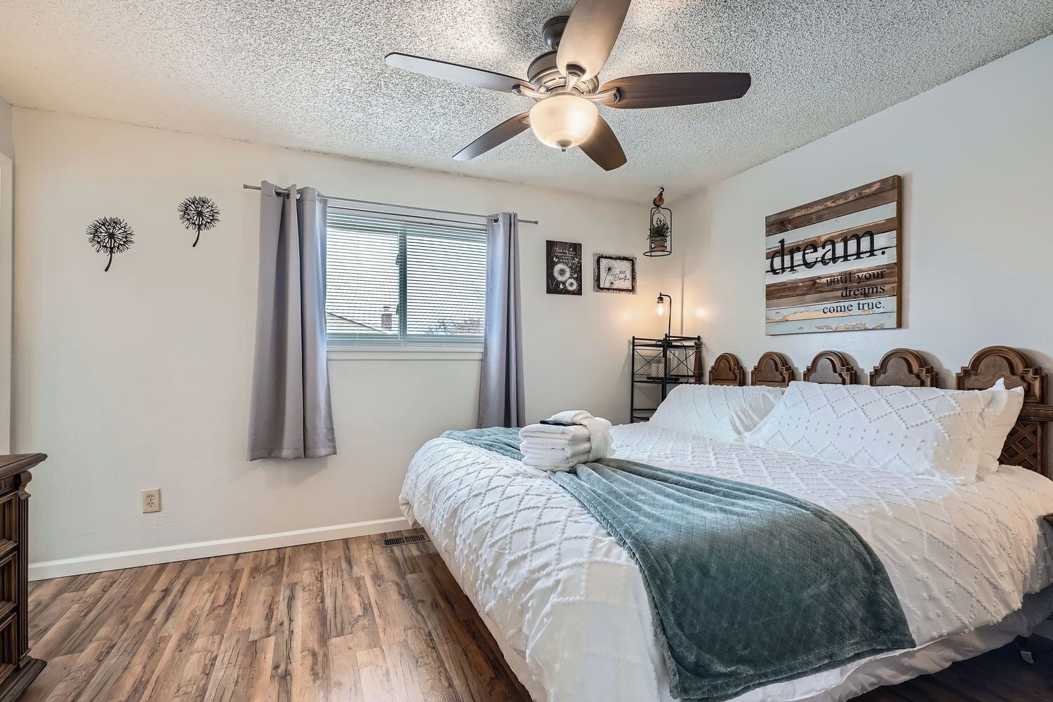 A bedroom with a bed, a ceiling fan, a window with curtains, a bedside table, and a wall decoration.