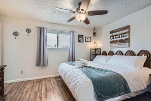 A bedroom with a bed, a ceiling fan, a window with curtains, a bedside table, and a wall decoration. - 3BR Westminster Home with Hot Tub, Yard + King Suite (Westminster)