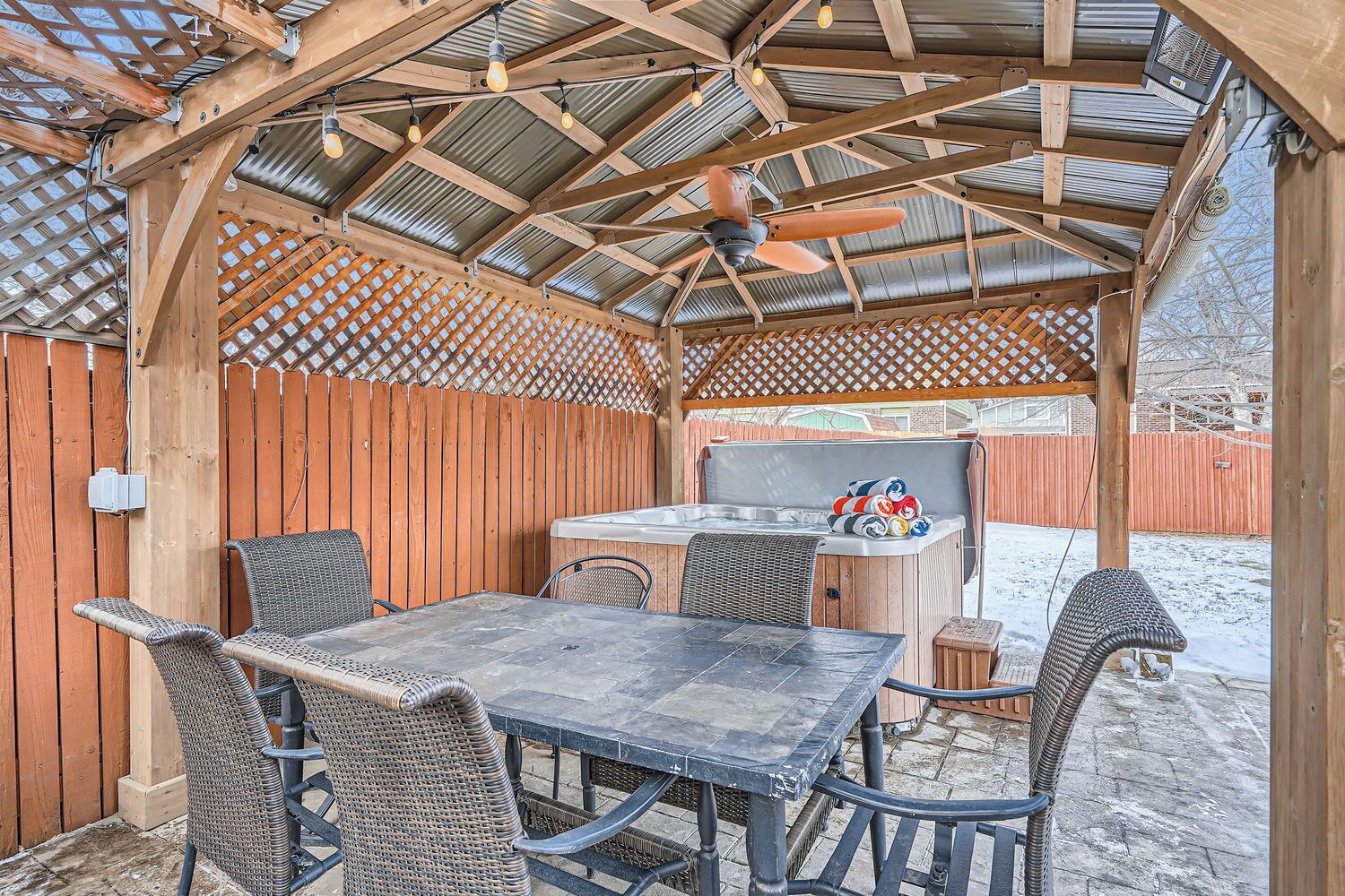 A covered outdoor patio with a table and chairs, a hot tub, and a ceiling fan.