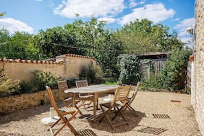 An outdoor patio with a wooden table and chairs, surrounded by gravel and greenery. - Cottage 'Gîte Les Hirondelles' with Shared Pool, Private Terrace and Wi-Fi (La Devise)