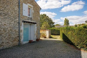 A stone building with a gravel driveway, a closed shutter door, and a window with shutters.