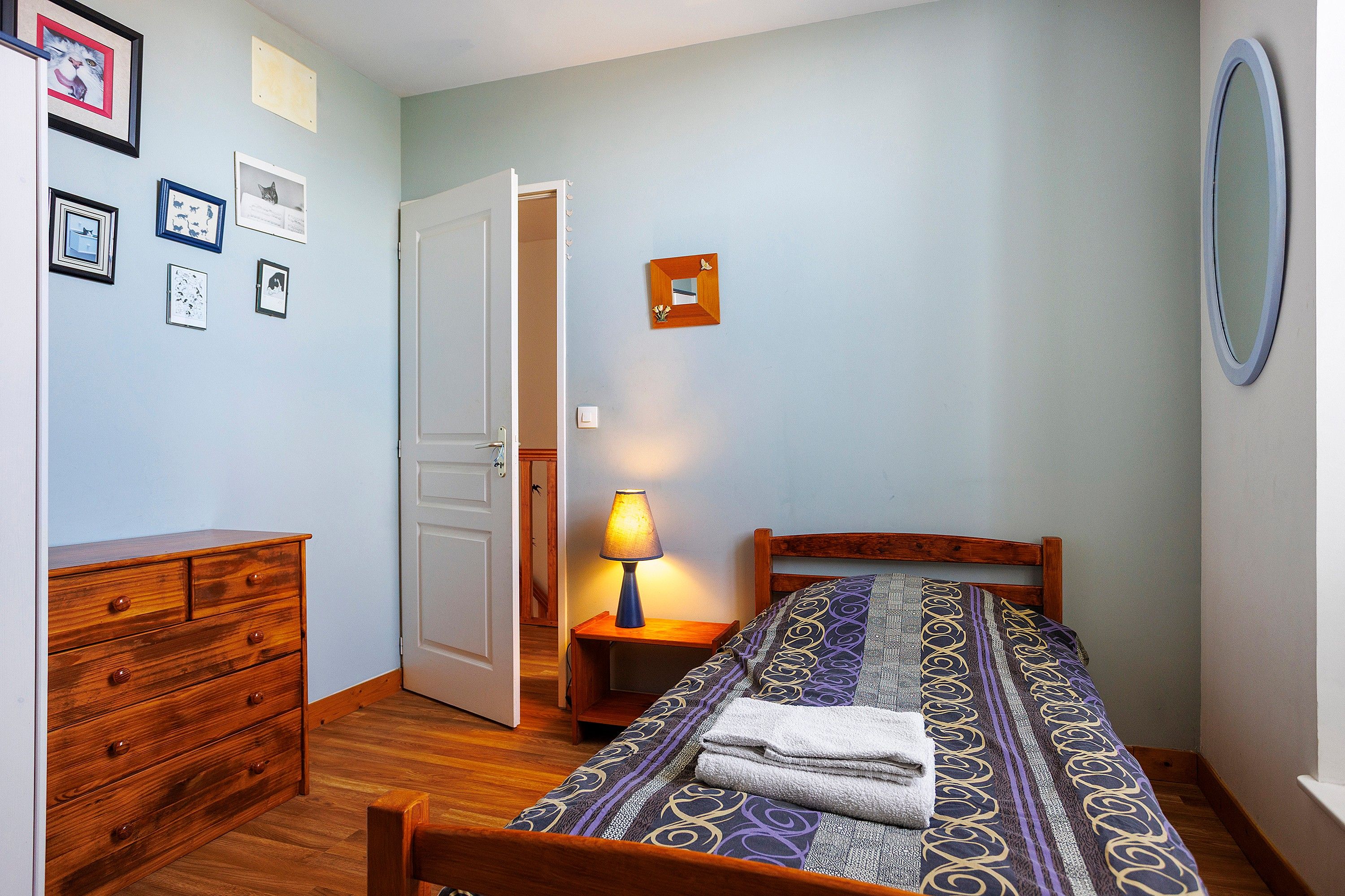 Une chambre à coucher avec un lit en bois, une table de chevet avec une lampe, une commode et une porte donnant sur une autre pièce.