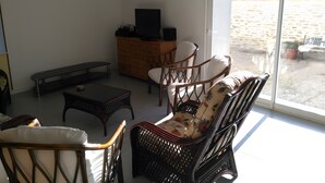 A living room with wicker furniture, a television on a wooden cabinet, and a view of a garden through a glass door.