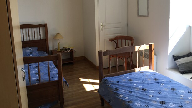 A bedroom with two wooden beds, a nightstand with a lamp, a chair, and a door.