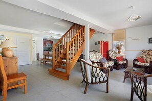 Un vaste espace de vie agrémenté d’un escalier en bois, de meubles en osier et d’une cuisine située au fond de la pièce.