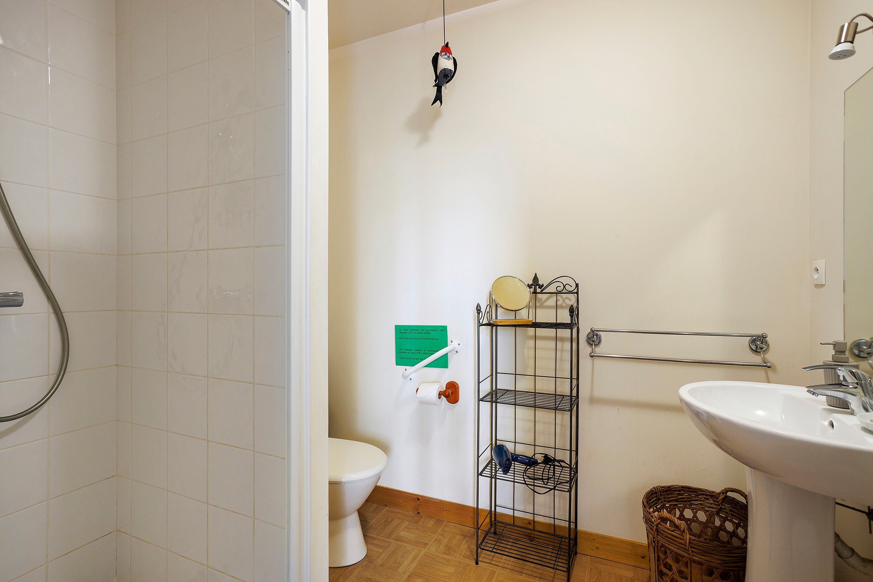 Un baño con inodoro, lavamanos, ducha y un estante metálico con un espejo y un pequeño repisa.