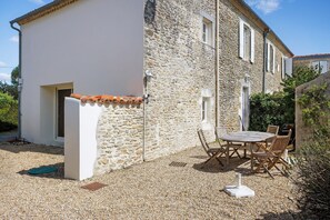 A two-story stone building with a white exterior and a tiled roof. There is a small patio with a round table and four chairs.