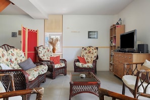 A living room with wicker furniture, a television, and a bookshelf. - Cottage 'Gîte Les Hirondelles' with Shared Pool, Private Terrace and Wi-Fi (La Devise)