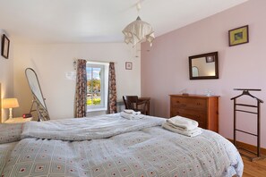 Une chambre à coucher comprenant un lit, une commode, un miroir et un luminaire suspendu.
