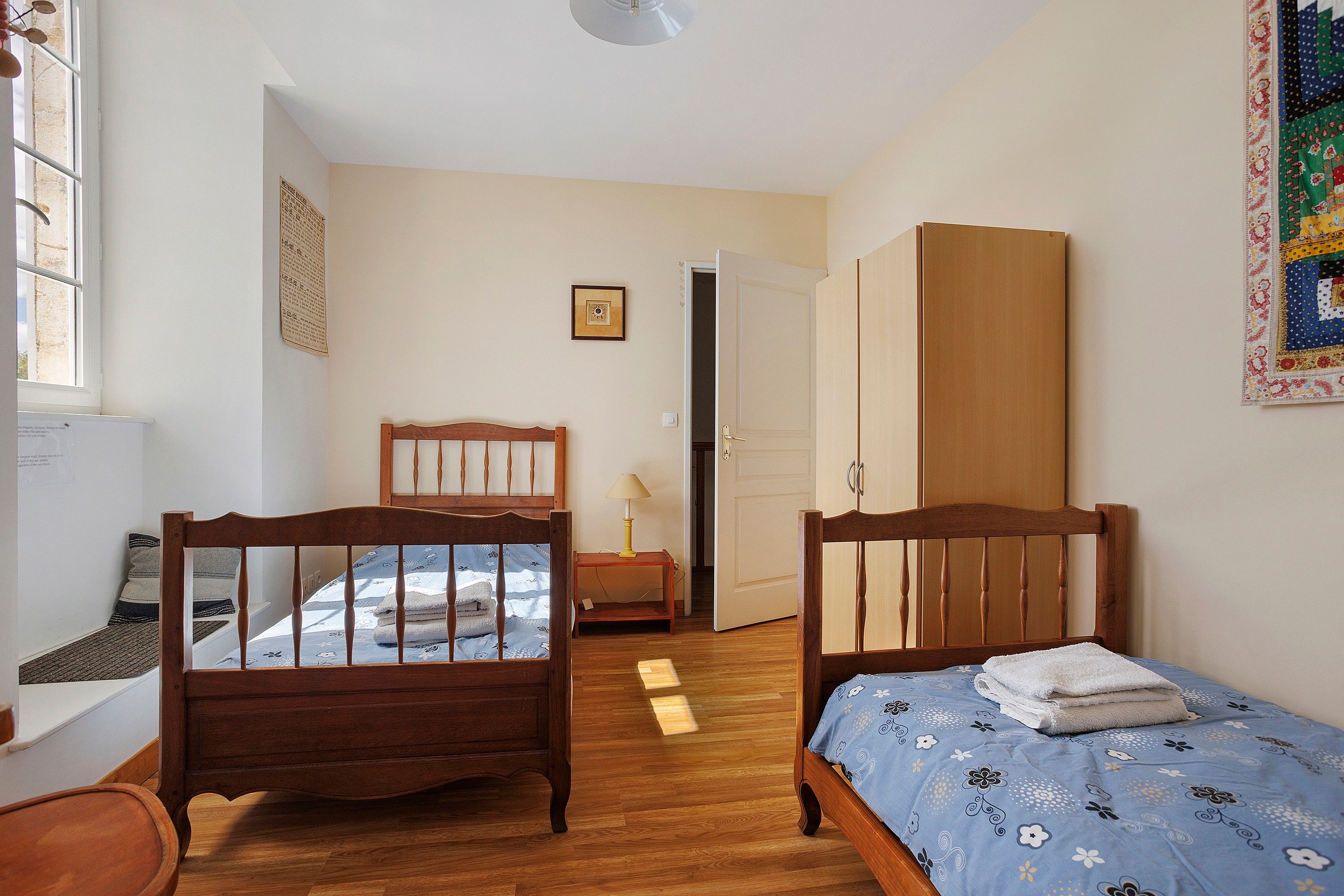 Una camera da letto con due letti in legno, un armadio, un comodino con una lampada e una finestra.