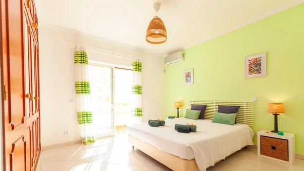 A bedroom with a bed, bedside tables, a hanging light fixture, and a window with curtains. - Elegant villa with pool in Galé (Albufeira)
