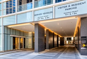 A modern building entrance with service vehicle and visitor parking signs, a glass facade, and a well-lit interior. - Tripshine Suites- Next to Rogers Center, MTCC&CN Tower (Toronto)