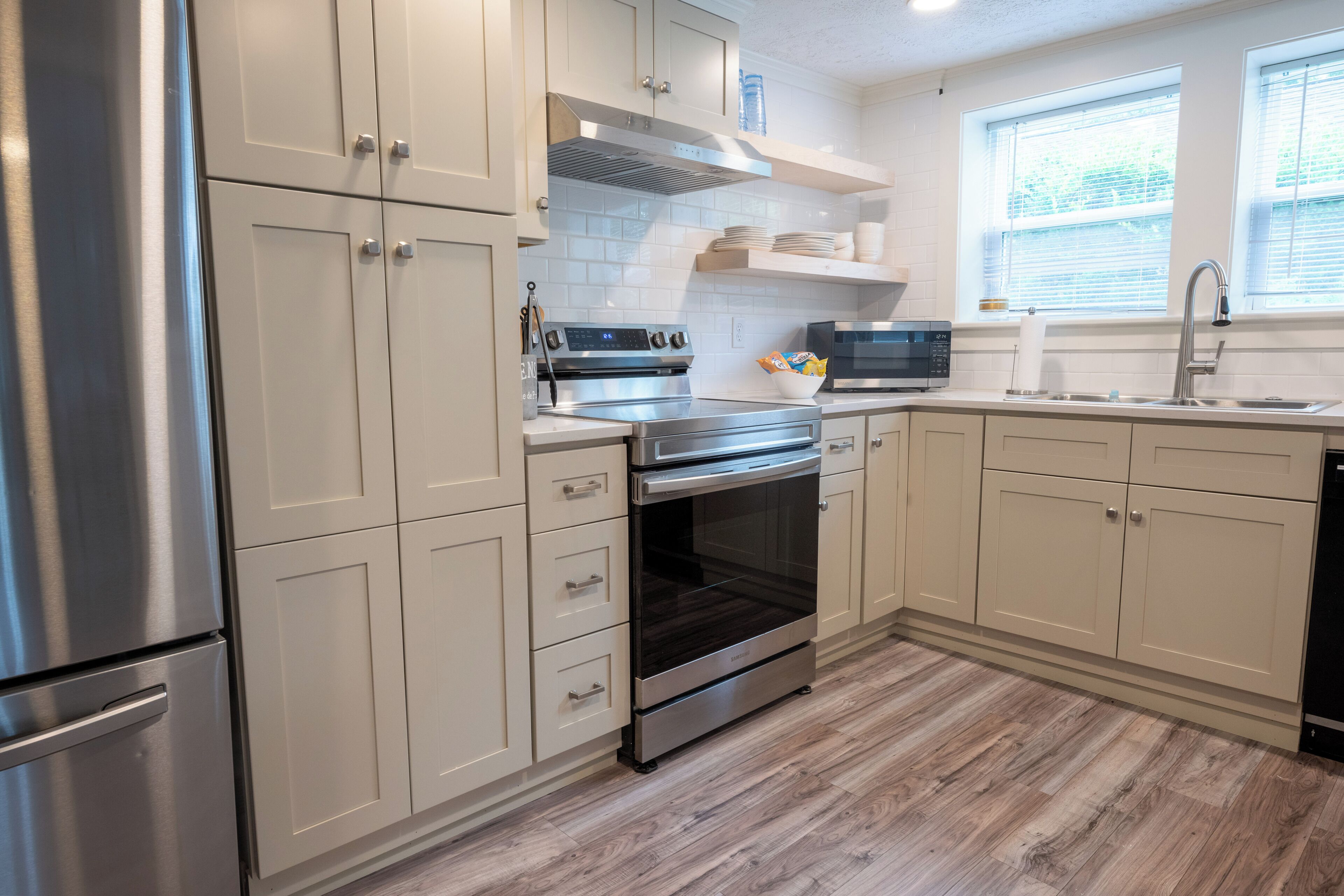 Cocina moderna con electrodomésticos de acero inoxidable, armarios blancos y suelo de madera.