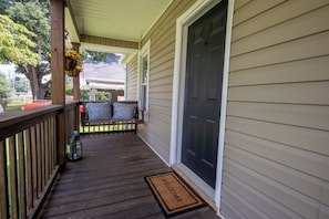 A wooden porch with a bench, a welcome mat, and a door.