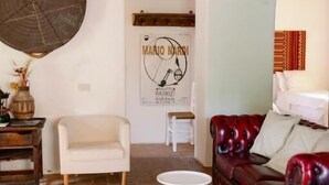 A room with a wooden ceiling, a chandelier, a round rug, a white chair, a red leather sofa, and a poster on the wall. - AGRITURISMO QUARANTALLINA (Buonconvento)