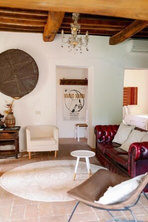 Una habitación con techo de madera, una araña, un tapete redondo, una silla blanca, un sofá de cuero rojo y un cartel en la pared.