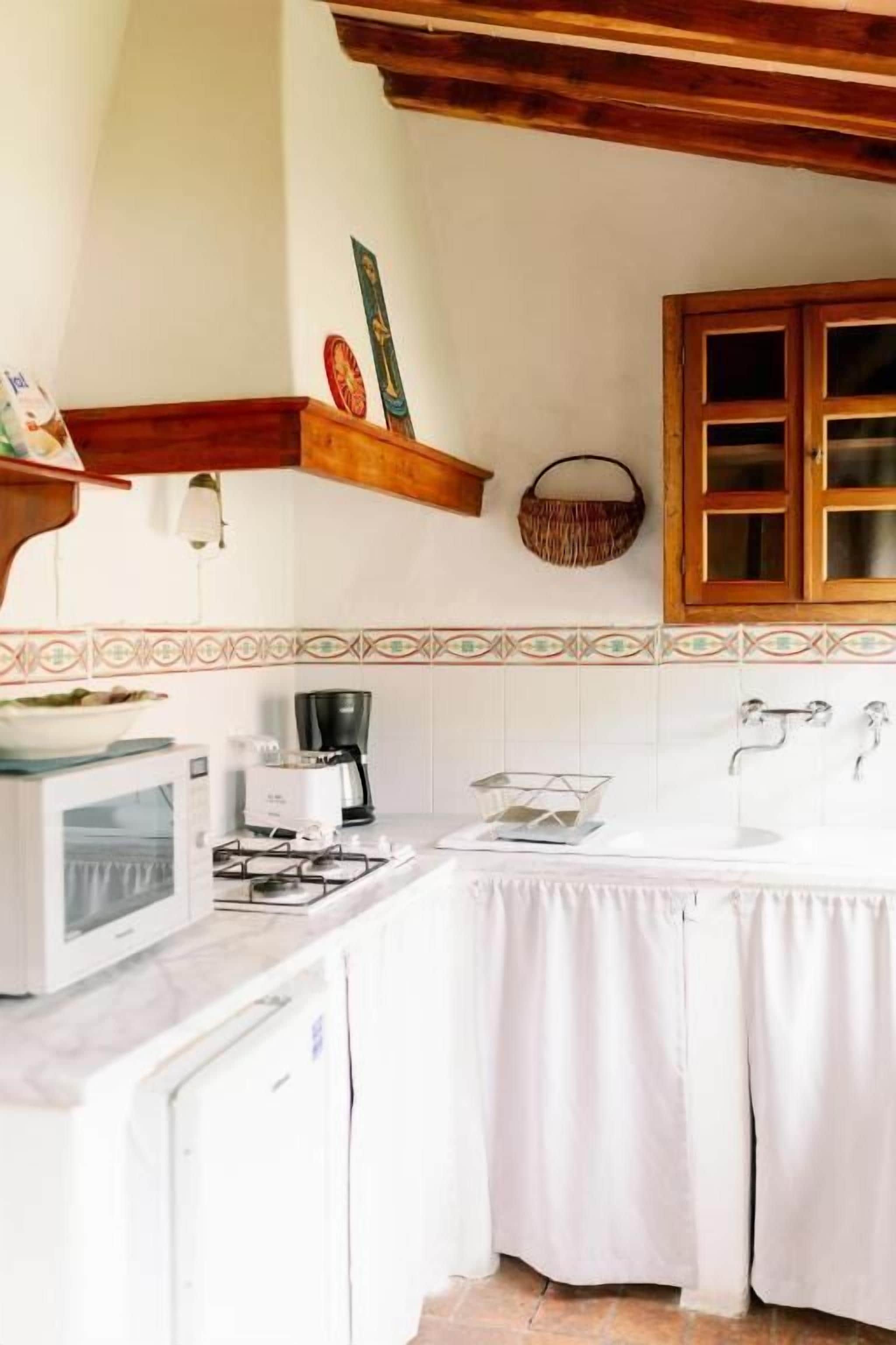 A kitchen with a microwave, stove, and coffee maker. There is a wooden shelf above the stove and a basket on the wall.