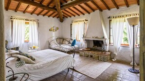 A bedroom with a bed, a fireplace, and a stone fireplace surround. - AGRITURISMO QUARANTALLINA (Buonconvento)