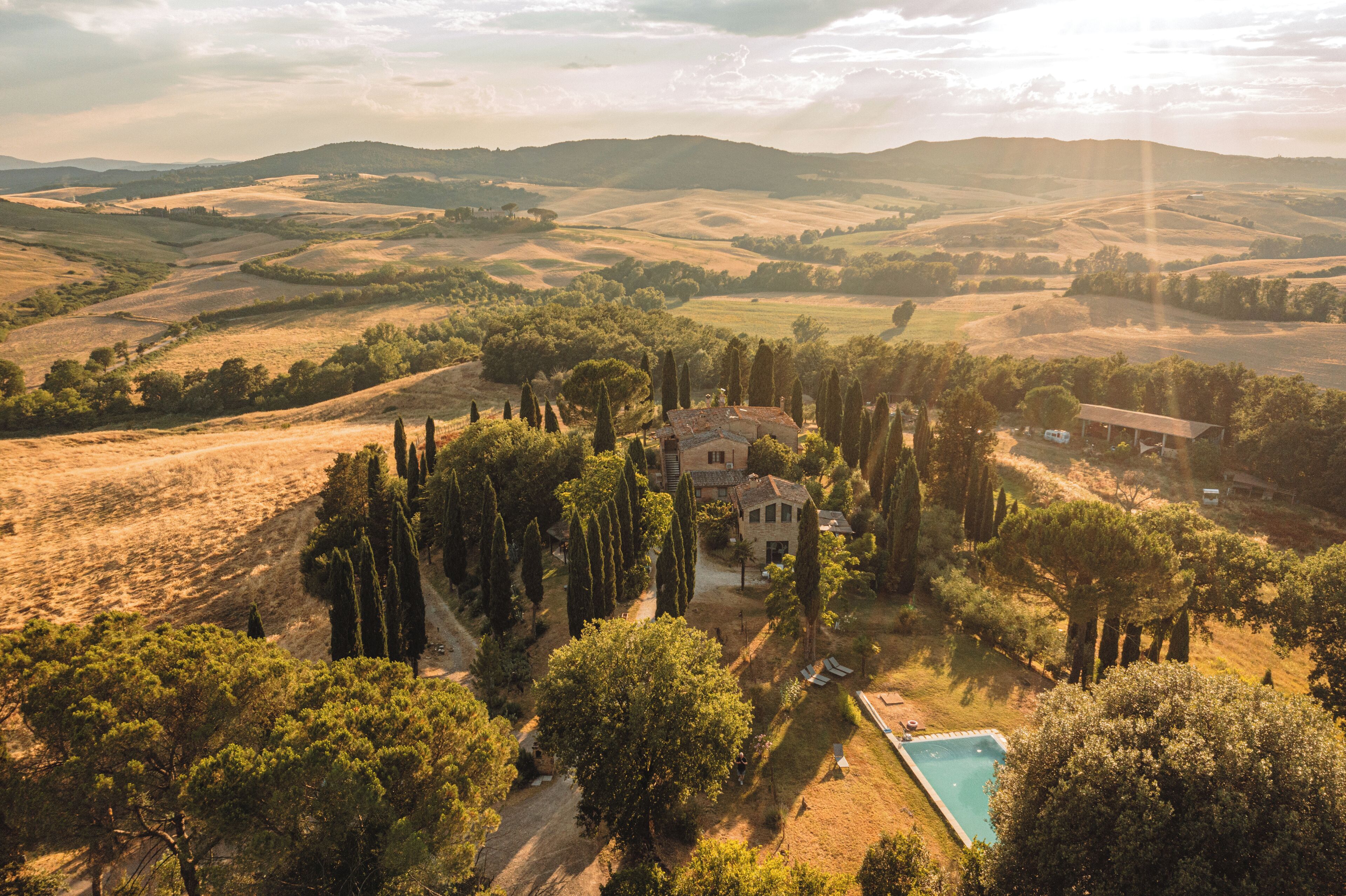 A villa surrounded by trees and hills, with a swimming pool in the foreground.