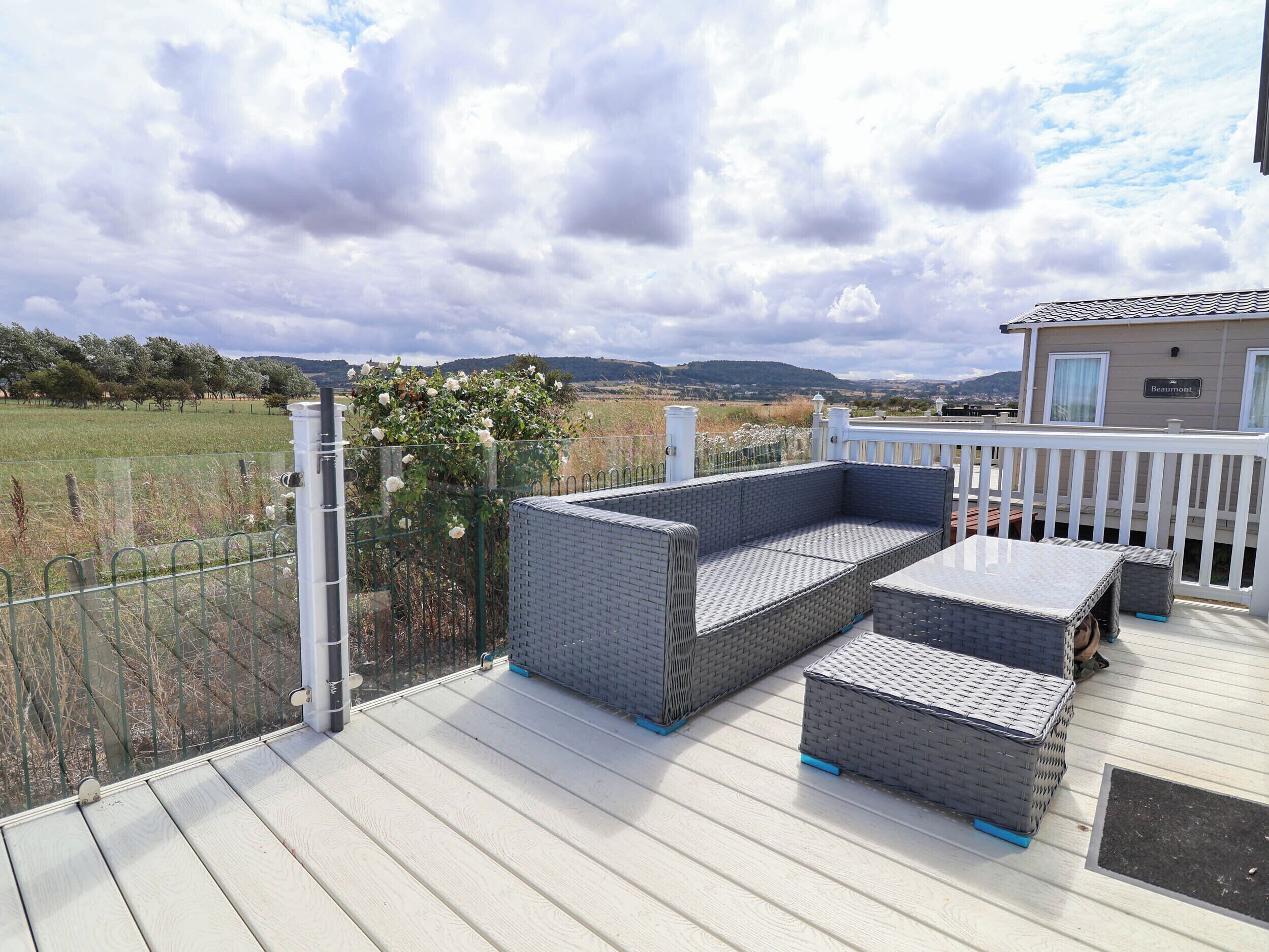 Una terraza con mobiliario exterior, cerca blanca y vista a un campo y colinas.
