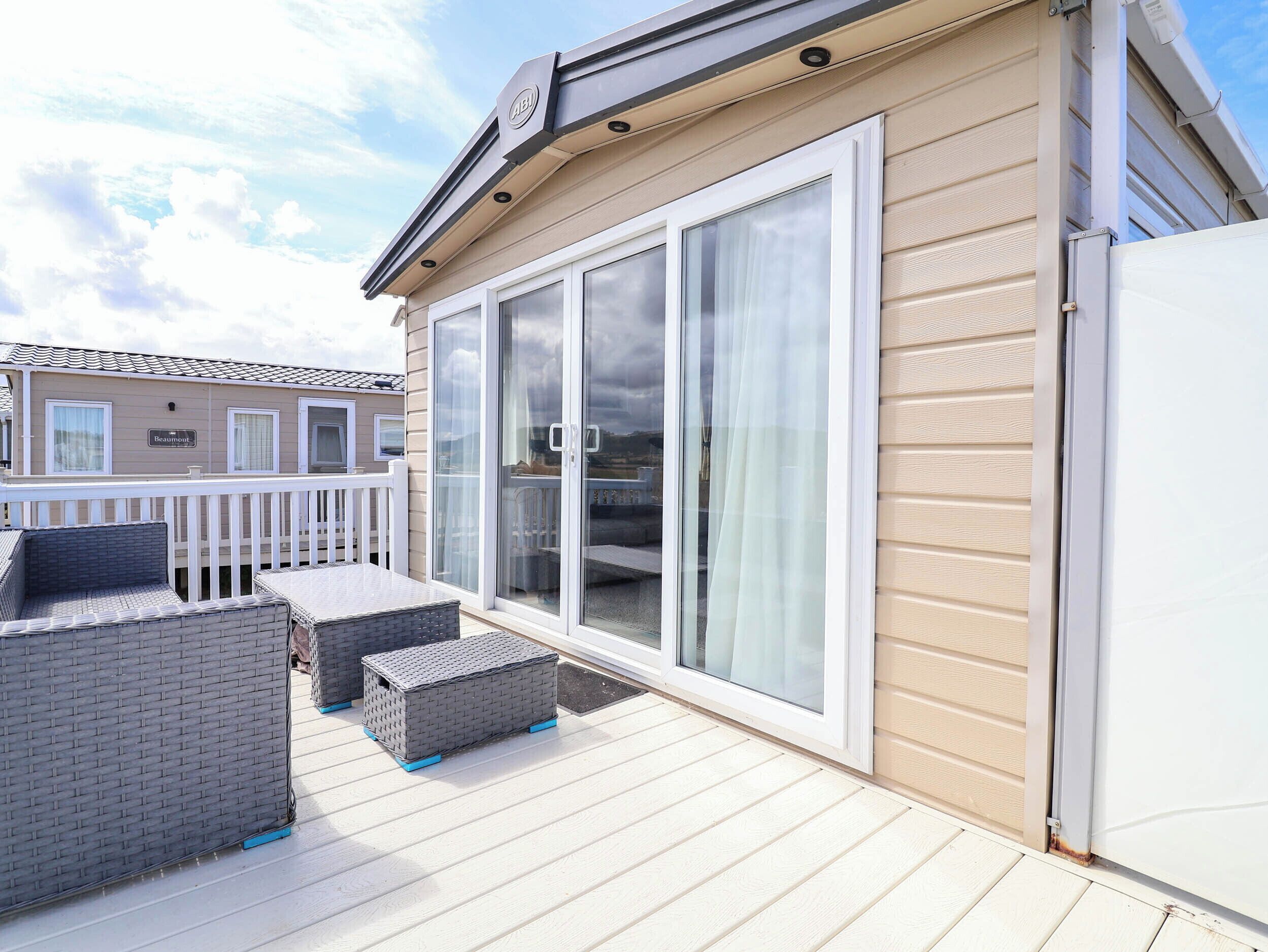 A covered outdoor deck with a sliding glass door, a white railing, and a table with chairs.