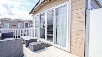A covered outdoor deck with a sliding glass door, a white railing, and a table with chairs.
