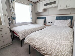 A bedroom with two beds, a wardrobe, and a window with curtains. - i35 - The Imperial (Abergele)