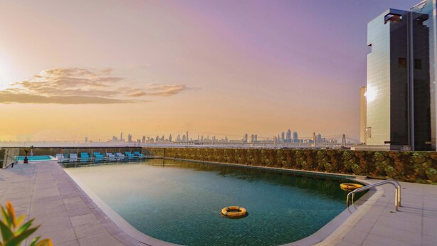 A rooftop swimming pool with a city skyline view, lounge chairs, and a lifebuoy. - Deluxe Escape  Luxury Wellness Hotel (Jumeirah Village Triangle)