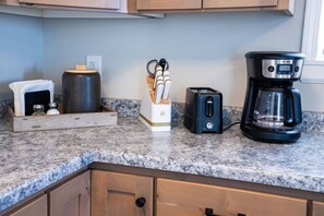 Un plan de travail de cuisine avec une machine à café, un grille-pain, des salières et des poivrières, et un bocal.