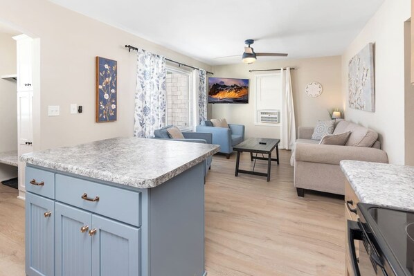 A modern kitchen with a marble countertop, a blue island with drawers, and a dining area with a table and chairs. - Cozy 2 Bedroom Renovated Home (St. Cloud)