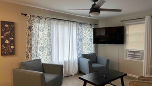 Ein Wohnzimmer mit zwei Sesseln, einem Couchtisch, einem Flachbildfernseher und einem Deckenventilator.