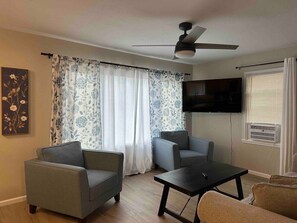 Ein Wohnzimmer mit zwei Sesseln, einem Couchtisch, einem Flachbildfernseher und einem Deckenventilator.