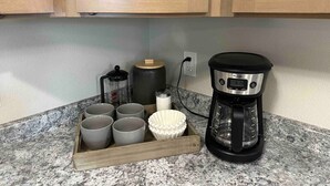 Eine Küchenarbeitsplatte mit Kaffeemaschine, einem Tablett mit Tassen, einer Aufbewahrungsbox und einem Wasserkocher.