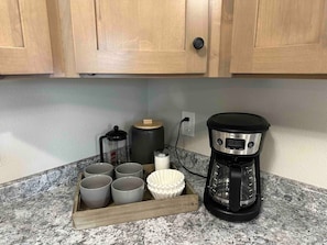 Eine Küchenarbeitsplatte mit Kaffeemaschine, einem Tablett mit Tassen, einer Aufbewahrungsbox und einem Wasserkocher.