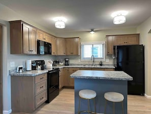 A kitchen with wooden cabinets, a black refrigerator, a stove, and a sink. - Cozy 2 Bedroom Renovated Home (St. Cloud)