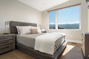 Un dormitorio con una cama grande, mesitas de noche, un aparador y una ventana con vistas a la montaña.