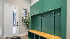 A hallway with a bench, a door, and a green wall with hooks. - Luxury Emerald Escape | Hot Tub | Ski Shuttle (Winter Park)