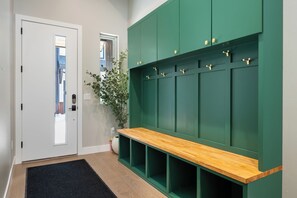 Um corredor com um banco, uma porta e uma parede verde com ganchos.