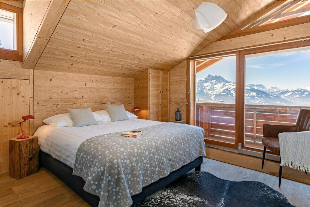 Une chambre à coucher située dans une cabane en bois, avec un lit, une table de chevet, une chaise et une vue sur les montagnes.