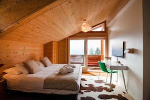 Un dormitorio con cama, escritorio y silla. Se ve una ventana con vistas a árboles.