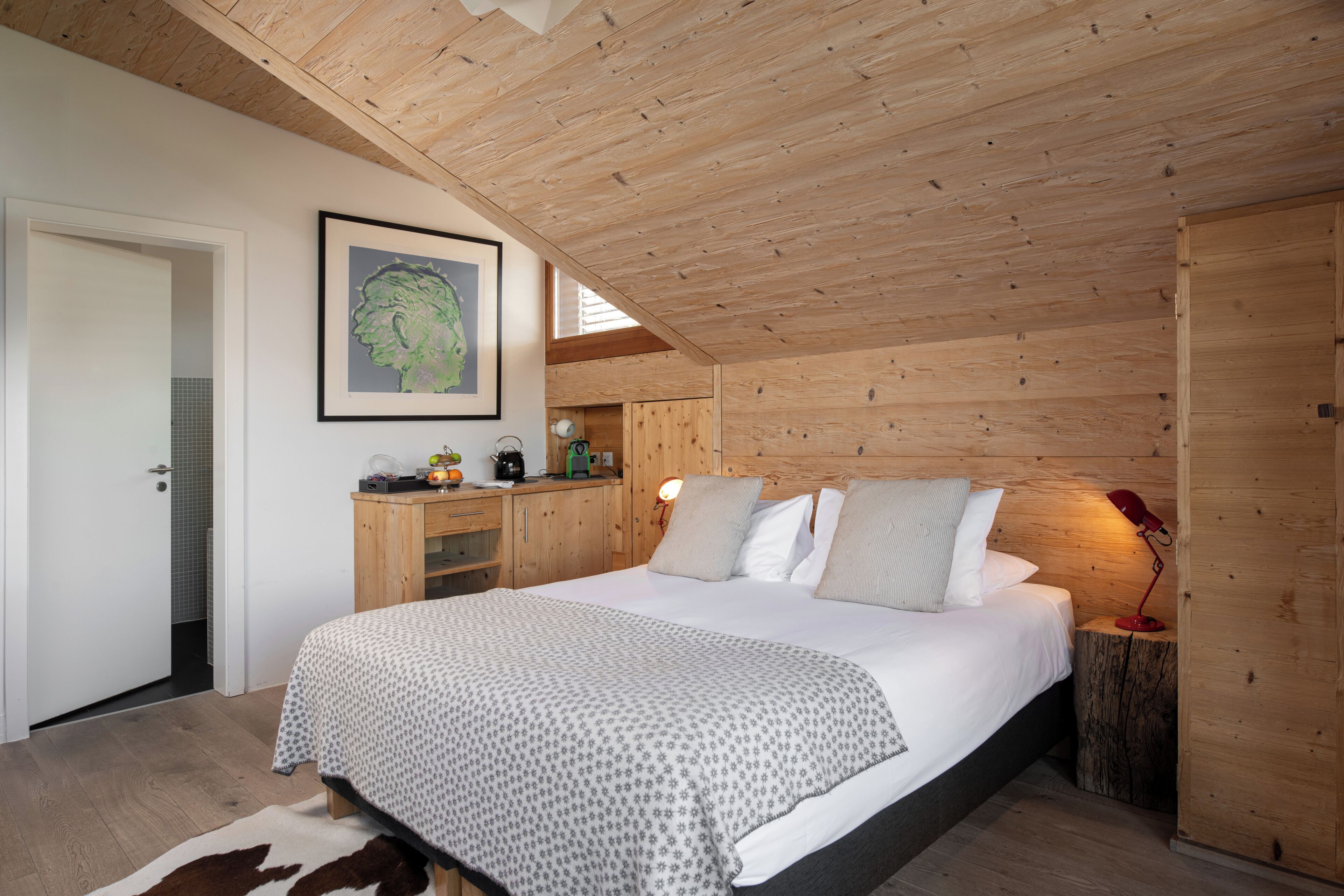 Ein Schlafzimmer mit Holzboden, einem Bett mit weißer Bettwäsche, einem Nachttisch mit Lampe und einem gerahmten Bild an der Wand.