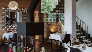 En restauranginteriör med bord, stolar, en öppen spis och en trappa.
