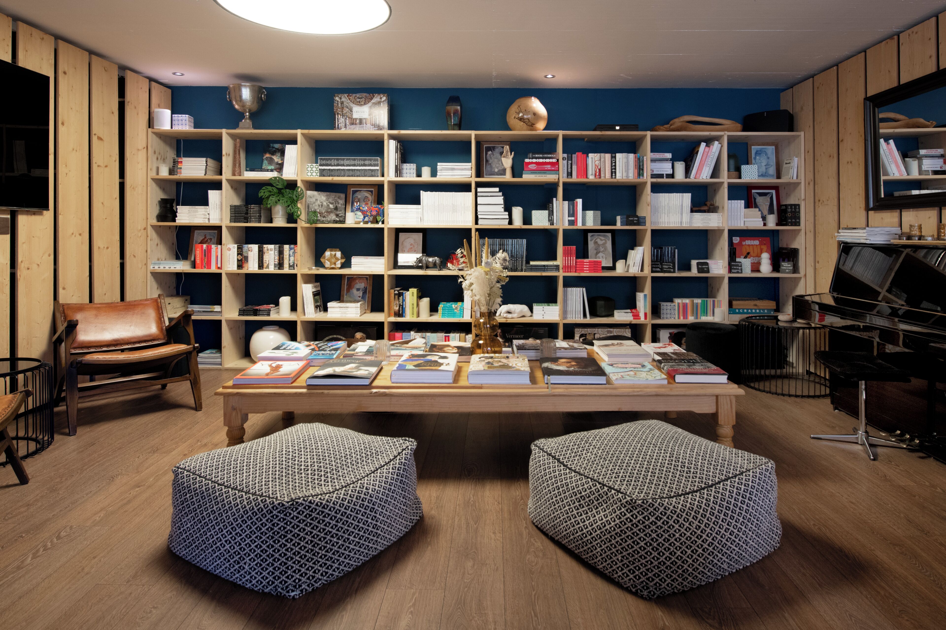 Une pièce avec une bibliothèque en bois remplie de livres, un fauteuil en cuir, une table basse sur laquelle sont posés des livres et des poufs à motifs.