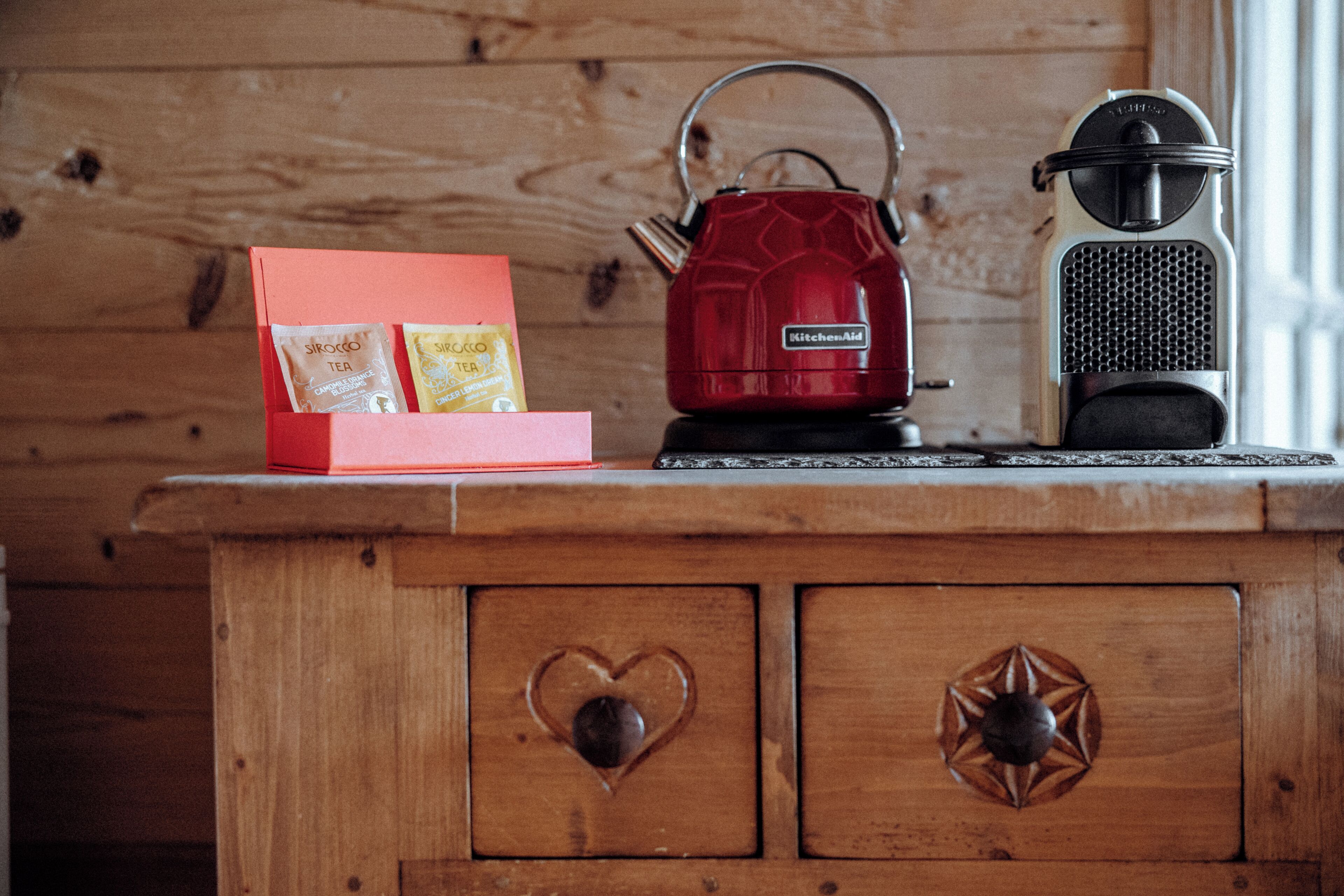 A wooden cabinet with two drawers, a red kettle, and a vintage radio.