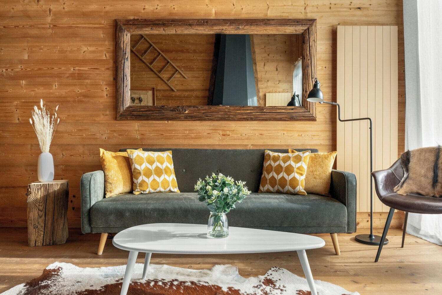 A cozy living room with a grey sofa, yellow patterned cushions, a white coffee table, and a wooden floor.