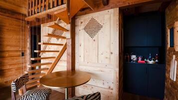 A wooden interior with a spiral staircase, a round table, zebra-patterned chairs, and a dark-colored cabinet.